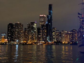 Illuminated buildings by river against sky at night