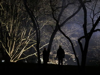 Silhouette man and woman standing amidst trees on field at night