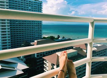 Low section of woman in red nail polish on railing against sea on sunny day