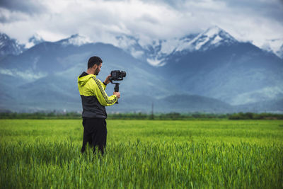 Man holding camera on a stabilizer on a green field ,scenic background