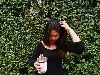 Young woman having drink while standing against plants