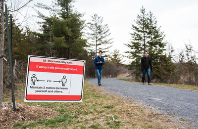 Man and teen boy walking on a wooded trail with covid 19 sign on it.