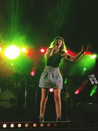 Full length of woman standing against illuminated lighting equipment