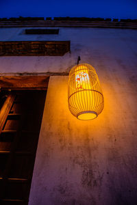 Low angle view of illuminated lamp hanging on wall at night