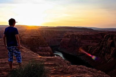 Rear view of boy standing on cliff against sky