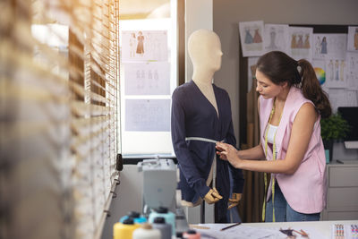 In her workplace, an asian tailor modifies the design of a garment on a mannequin.