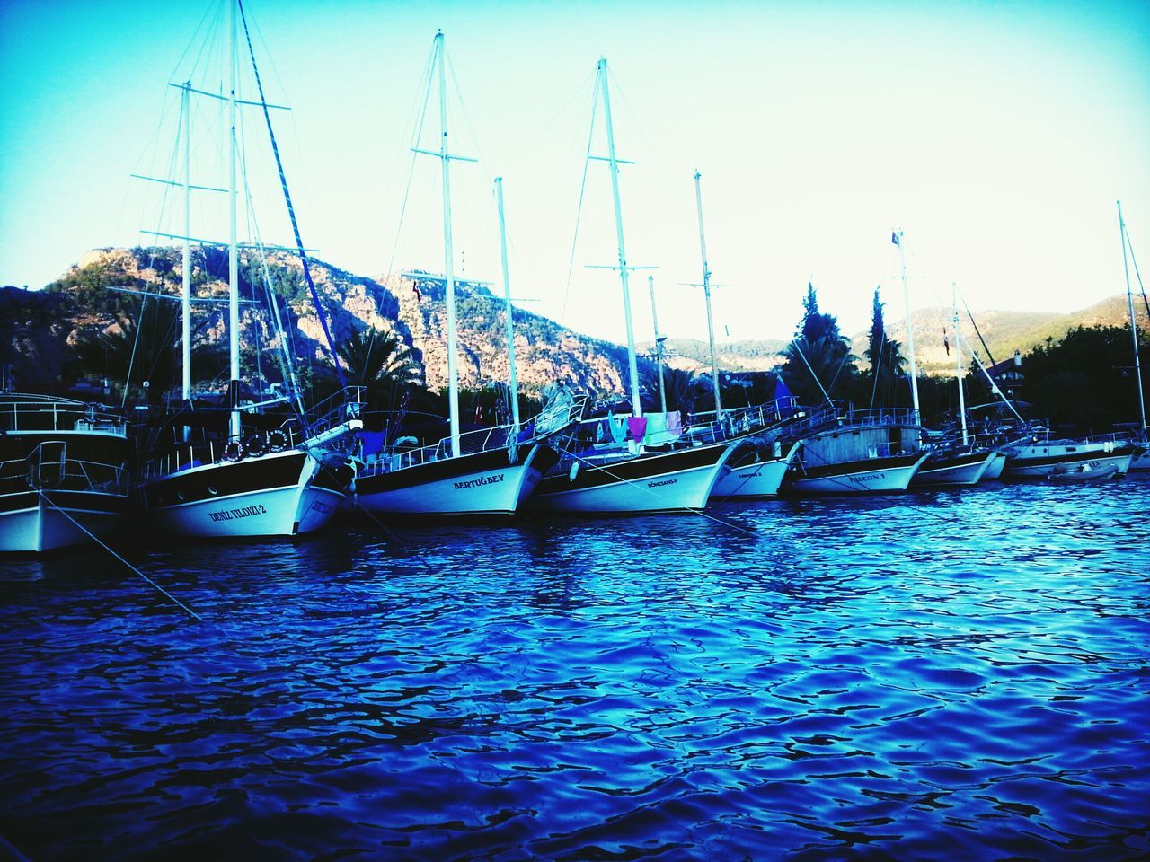 water, built structure, blue, river, transportation, waterfront, architecture, connection, nautical vessel, clear sky, bridge - man made structure, sky, boat, mast, rippled, harbor, building exterior, mode of transport, moored, city