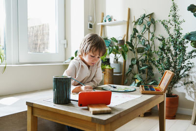 Preschooler boy using digital tablet art drawing multicolored image use paints and brush on table