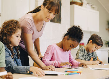 Teacher guiding male and female students at desk in classroom