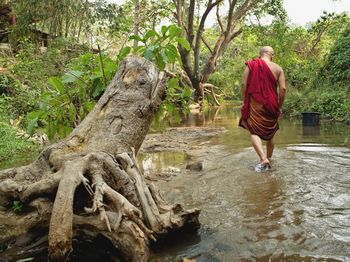 Full length of monk wading in lake at forest