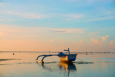 Outrigger moored in sea against sky during sunset