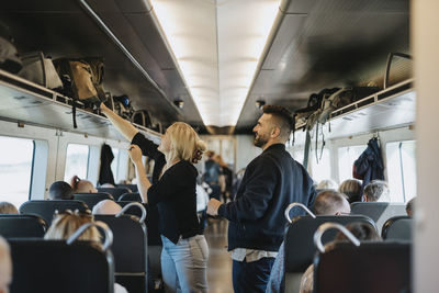 Woman helping man to load luggage on shelf in train