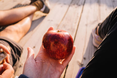 Low section of person having apple while sitting with friend on wooden floor