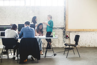 Female colleagues talking while professional hackers coding at desk in creative office