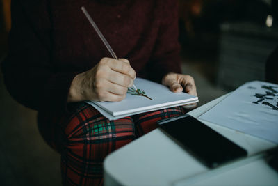 Midsection of woman holding paper while sitting on table