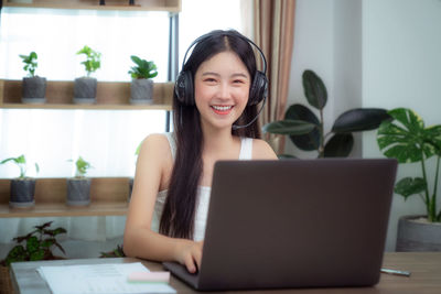 Portrait of smiling young woman using phone on table
