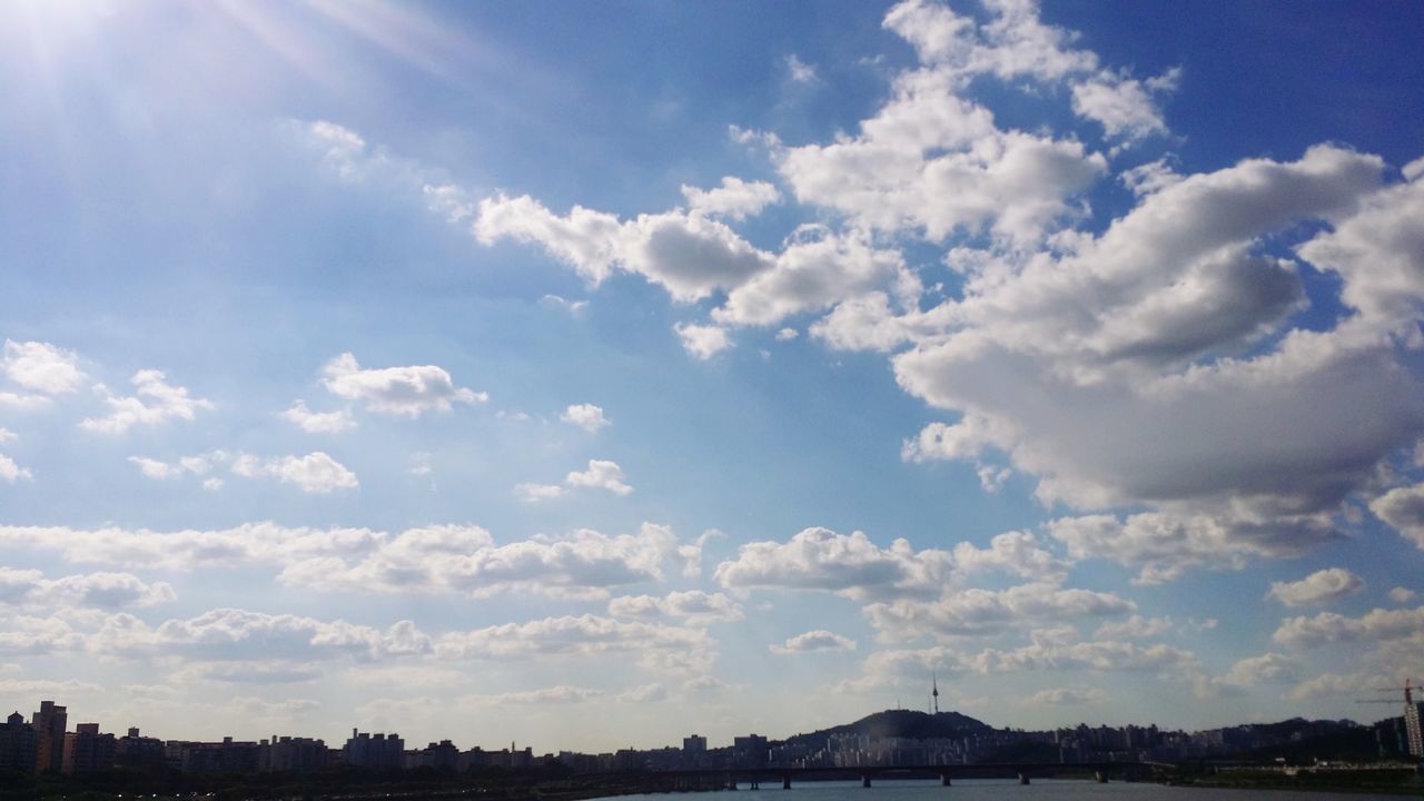 sky, cloud - sky, scenics, beauty in nature, cloud, tranquility, blue, tranquil scene, sunlight, nature, built structure, sunbeam, architecture, building exterior, city, cloudy, water, outdoors, no people, day