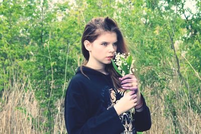 Woman smelling flowers while standing in forest