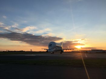 Airplane on airport runway against sky during sunset