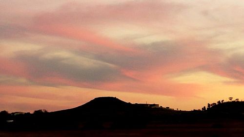 Scenic view of landscape against cloudy sky at sunset