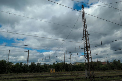 Electricity pylon on field against cloudy sky