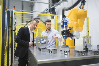 Two businessman observing industrial robots in factory