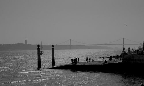 Silhouette people on bridge over sea against clear sky