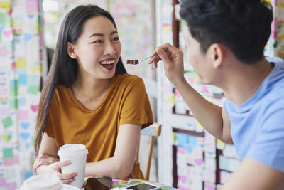 Man feeding happy girlfriend while sitting in restaurant