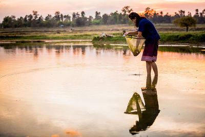 Side view of man standing by lake against sky