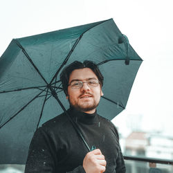 Portrait of man holding umbrella standing against sky