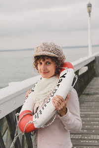 Portrait of happy woman with inflatable ring on pier against sky