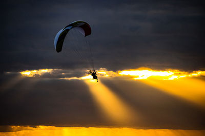 Silhouette person paragliding against sky during sunset