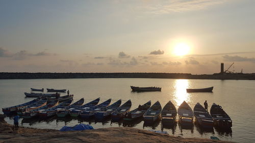 Boats moored side by side in river against sky during sunset