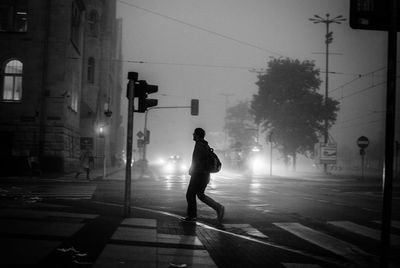 Side view of man walking on road by traffic lights and buildings