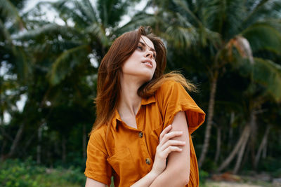 Young woman looking away against trees