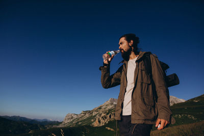 Full length of a man drinking water against clear blue sky