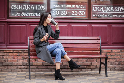 Full length of woman sitting on seat in city