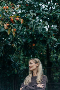Portrait of young woman standing against tree