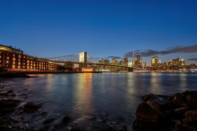 Illuminated bridge over river against clear blue sky