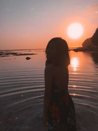 Silhouette young woman standing in sea against clear sky at sunset