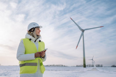 Engineer wearing hardhat holding smart phone standing at wind farm