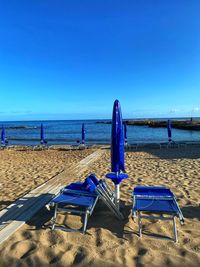 Deck chairs on beach against clear blue sky