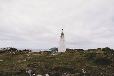 Lighthouse on field against cloudy sky