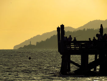 Silhouette people on sea against orange sky