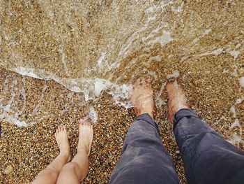 Low section of father with son standing on shore at beach