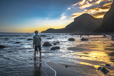 Rear view of man standing at beach during sunset