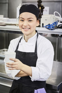 Portrait of smiling female chef holding disposable cup in commercial kitchen