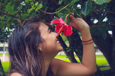 Smiling young woman smelling hibiscus flower at park