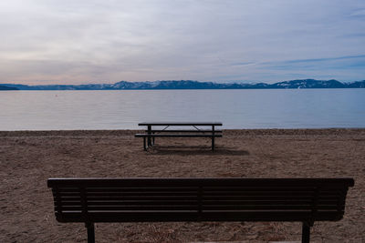 Empty bench on beach against sky