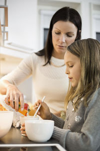 Mother and daughter adding flavor in cup at kitchen